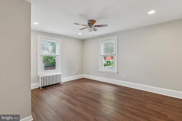 an empty room with wooden floor chandelier fan and windows