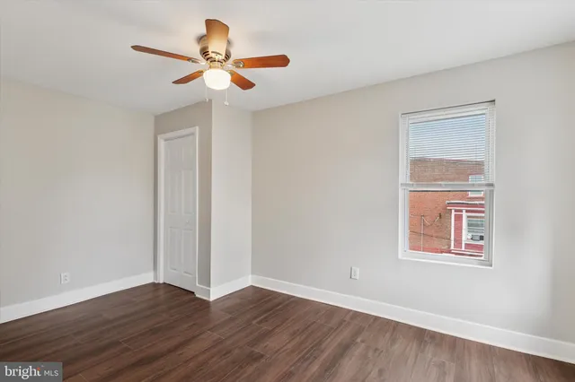 a view of an empty room with wooden floor and a ceiling fan