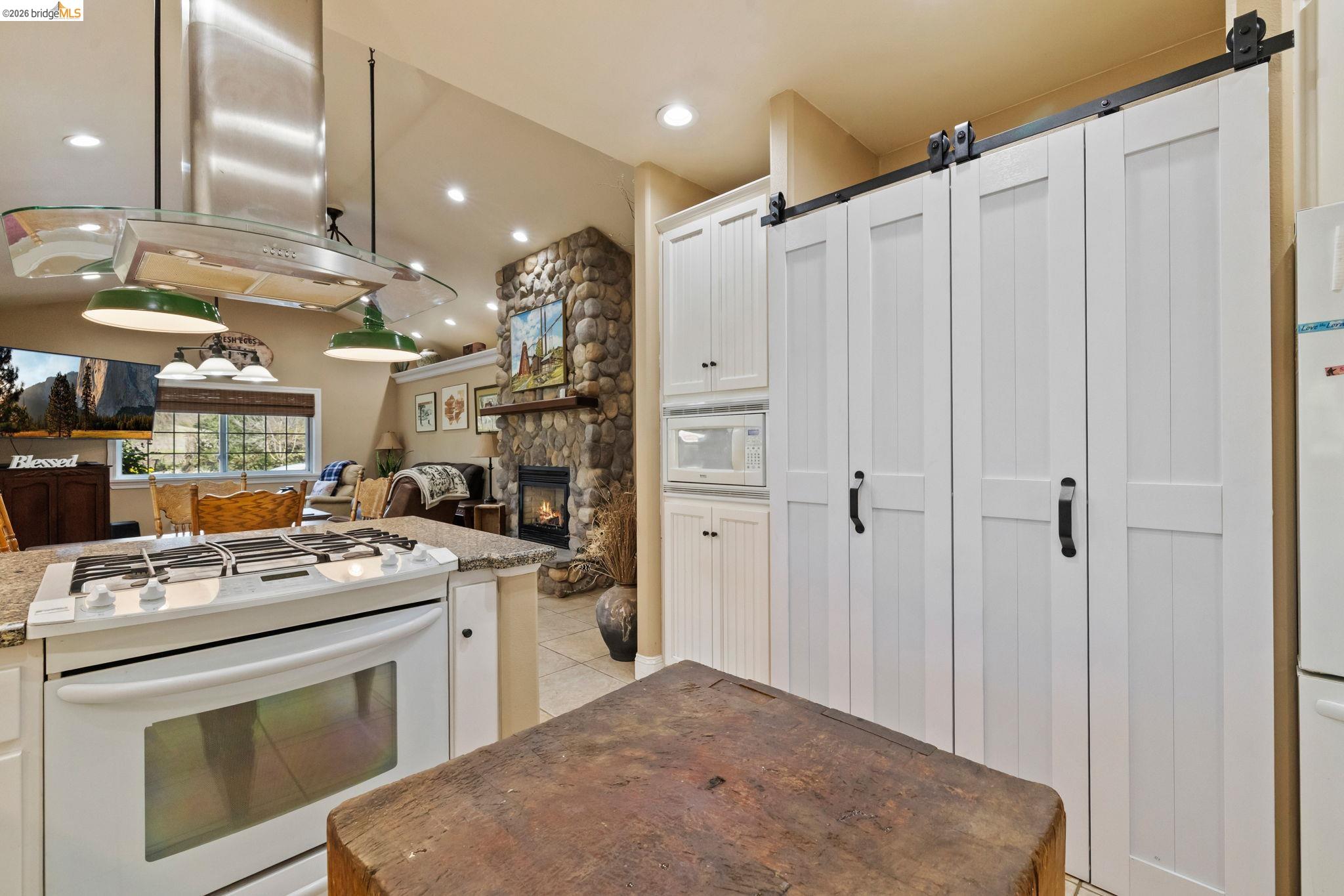 10177 Pulpit Rock Road Jamestown, CA 95327 - Photo 12 of 60 Kitchen featuring white appliances, white cabinetry, island range hood, light tile patterned flooring, and a fireplace