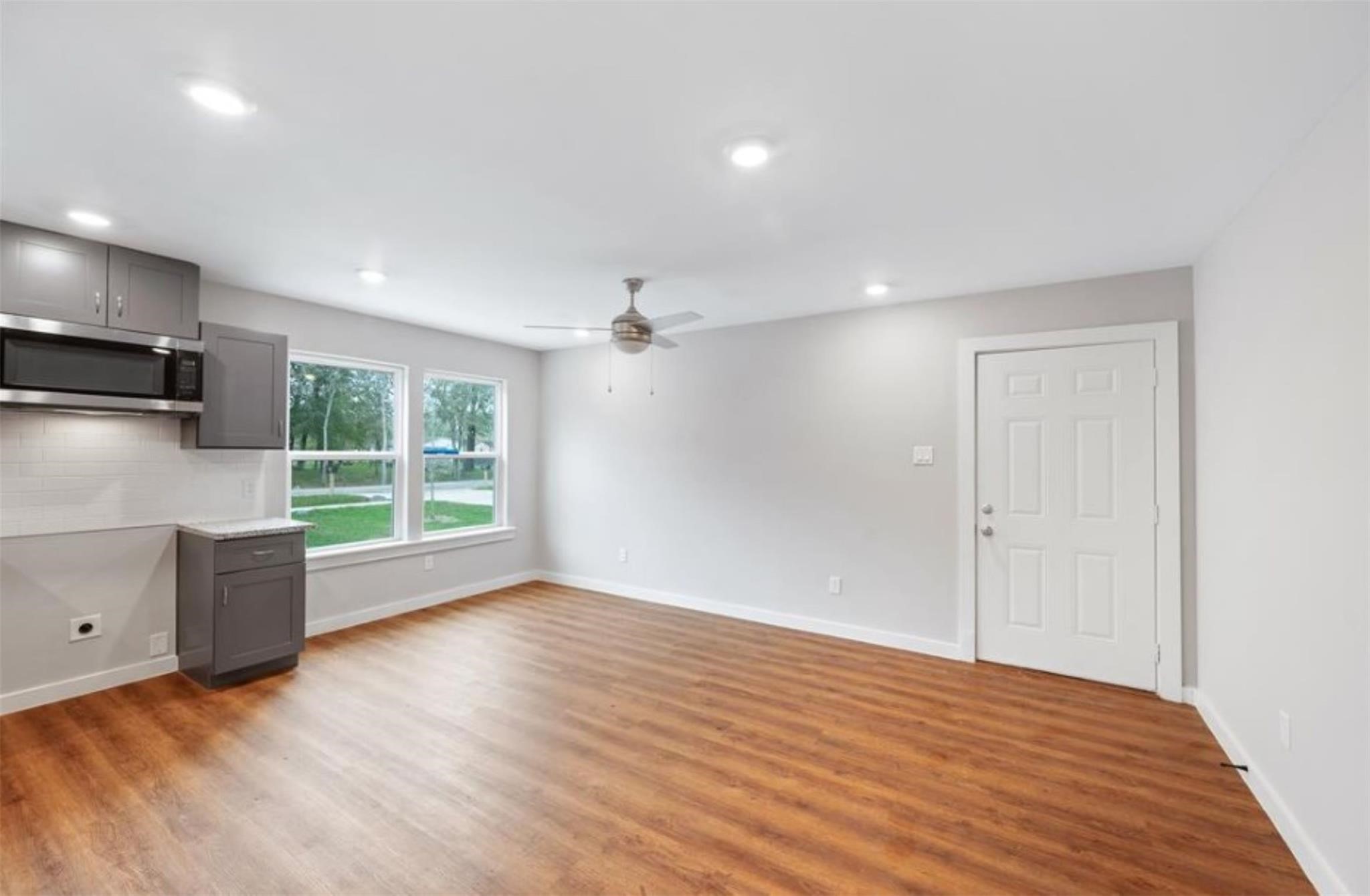 8120 Laura Koppe Road, Unit B Houston, TX 77028 - Photo 8 of 25 This bright, open-concept living area features wood flooring, modern gray cabinetry, and a sleek ceiling fan. Large windows provide ample natural light, and the room includes a compact kitchen area with a built-in microwave.