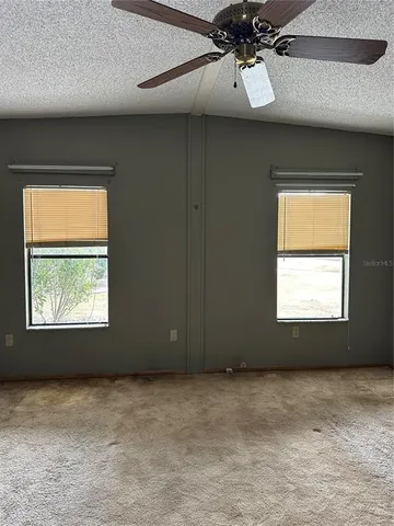 an empty room with a chandelier fan and windows