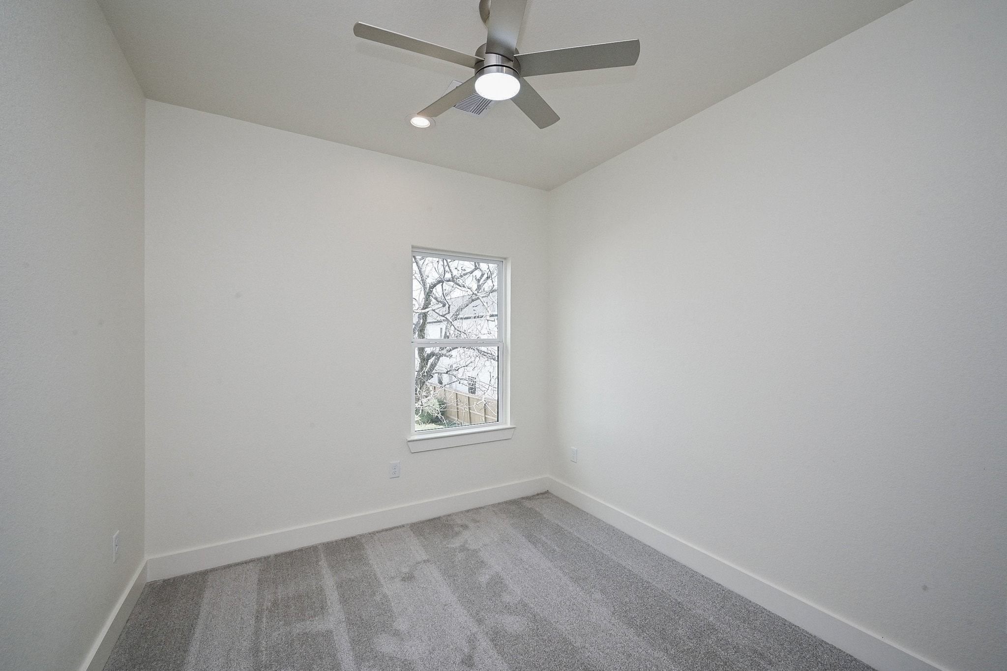 3839 Noah Street, Unit B Houston, TX 77021 - Photo 13 of 19 This is a bright, minimalist room featuring neutral walls, a gray carpet, and a modern ceiling fan. It has a window offering natural light, creating a cozy and inviting space.