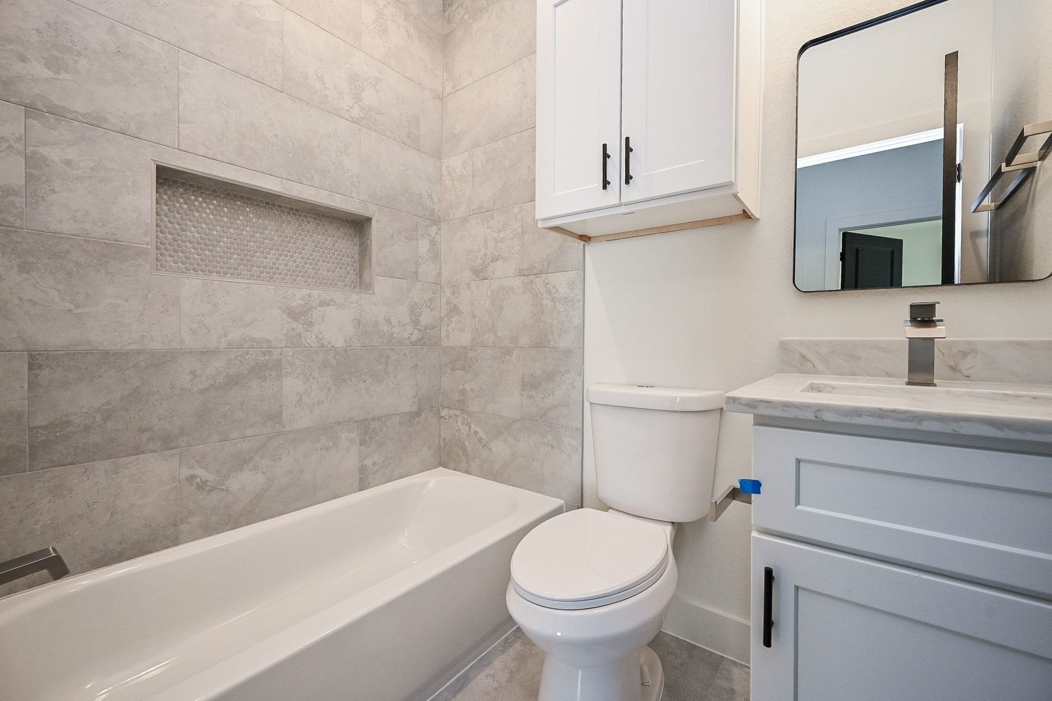 3839 Noah Street, Unit B Houston, TX 77021 - Photo 16 of 19 Modern bathroom featuring a sleek bathtub with gray tiled walls, a built-in niche, and a stylish vanity with a marble countertop. The space is complemented by a white cabinet and a contemporary mirror, creating a clean and functional look.