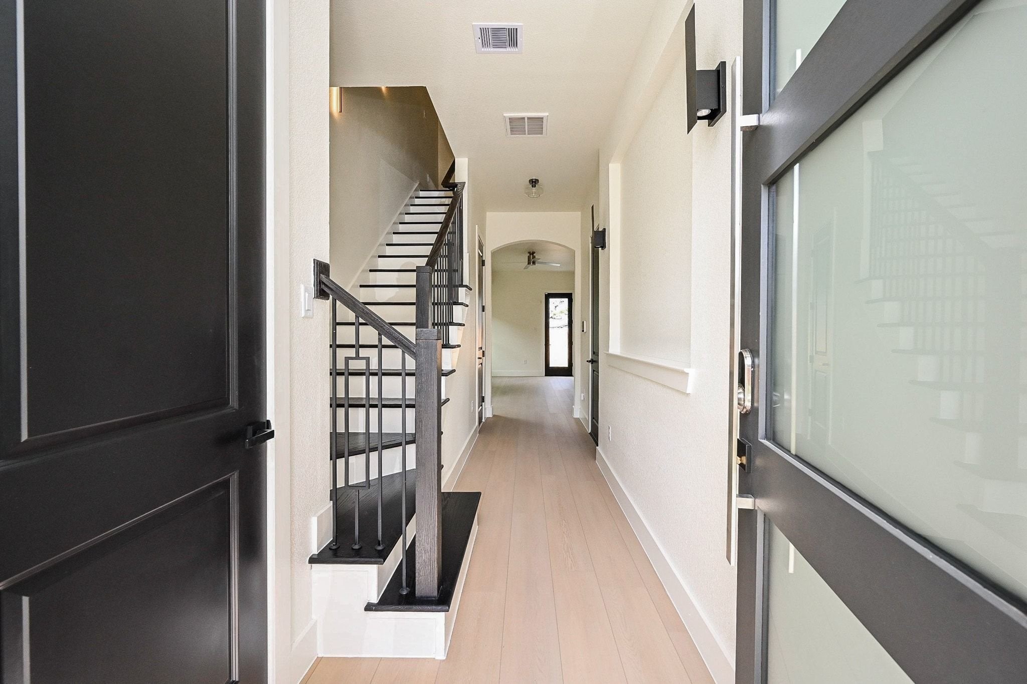 3839 Noah Street, Unit B Houston, TX 77021 - Photo 2 of 19 This photo showcases a modern entryway with light wood flooring and sleek black accents. The hallway leads to an open area, featuring a staircase with black railings and a glass-paneled front door. The space is bright, with contemporary lighting and a clean, minimalist design.