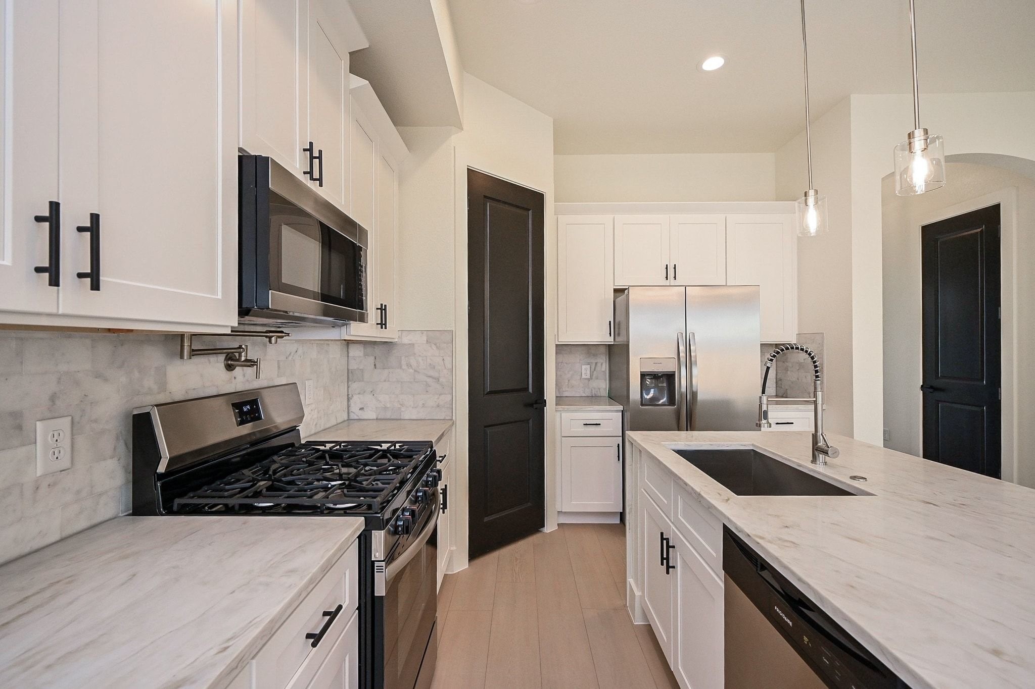 3839 Noah Street, Unit B Houston, TX 77021 - Photo 6 of 19 Modern kitchen with sleek white cabinetry, marble countertops, and stainless steel appliances, including a large fridge and gas stove. Features a central island with a sink and stylish pendant lighting, creating a clean and inviting space.