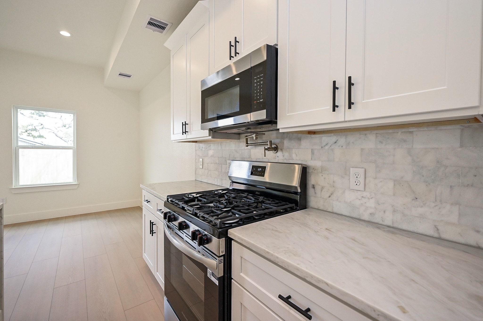 3839 Noah Street, Unit B Houston, TX 77021 - Photo 7 of 19 Modern kitchen with sleek white cabinetry, marble countertops, and stainless steel appliances, including a large fridge and gas stove. Features a central island with a sink and stylish pendant lighting, creating a clean and inviting space.