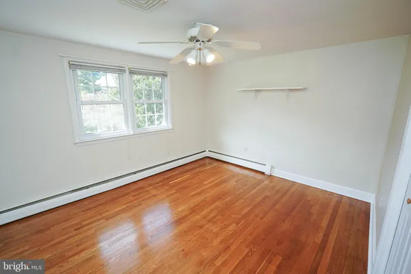 a view of an empty room with wooden floor and a ceiling fan