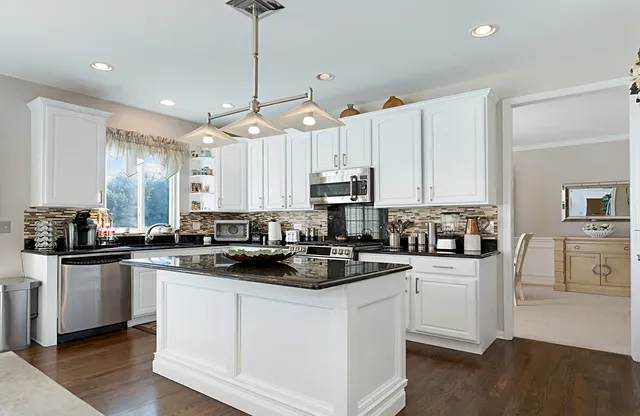 a kitchen with stainless steel appliances kitchen island granite countertop a sink a stove a refrigerator and white cabinets