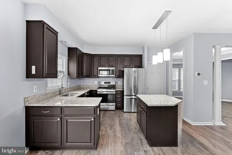 a kitchen with kitchen island granite countertop a stove top oven a sink dishwasher a dining table and chairs with wooden floor