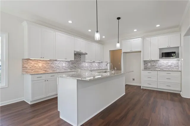 a kitchen with stainless steel appliances granite countertop a sink a stove a refrigerator and white cabinets with wooden floor