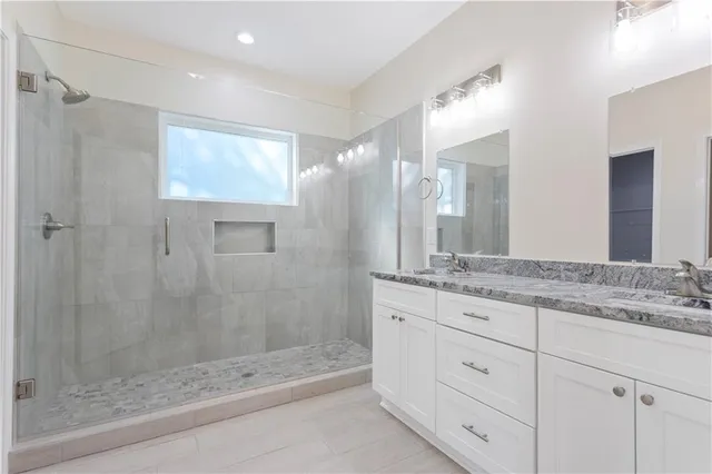 a bathroom with a granite countertop sink a mirror and a glass door shower