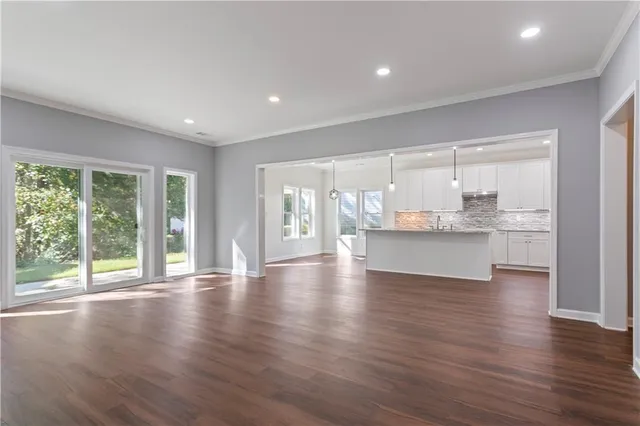 a view of an empty room with wooden floor and kitchen