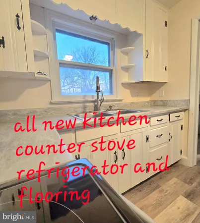 a kitchen with stainless steel appliances granite countertop a refrigerator a stove a sink and white cabinets with wooden floor