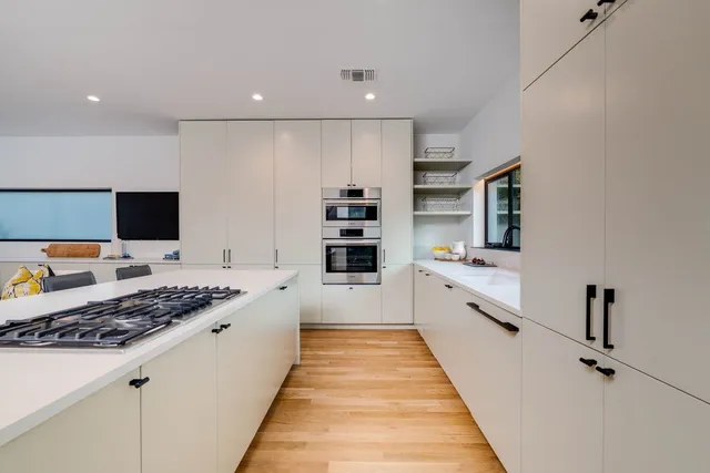 a large white kitchen with stainless steel appliances granite countertop a stove and a sink