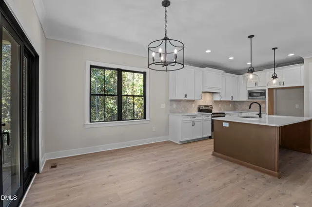 a kitchen with stainless steel appliances granite countertop a stove a sink dishwasher a refrigerator and white cabinets with wooden floor