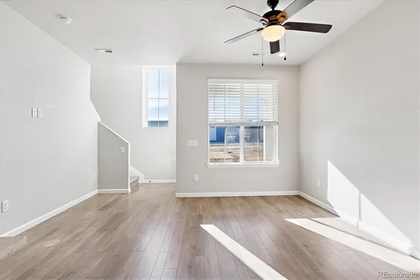 an empty room with wooden floor chandelier fan and windows