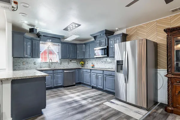 a kitchen with granite countertop a refrigerator a sink dishwasher a stove and white cabinets with wooden floor