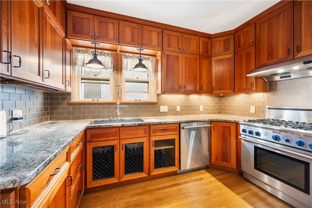 24510 Lake Road Bay Village, OH 44140 - Photo 20 of 45 Kitchen featuring appliances with stainless steel finishes, light wood-style flooring, tasteful backsplash, light stone counters, and brown cabinetry