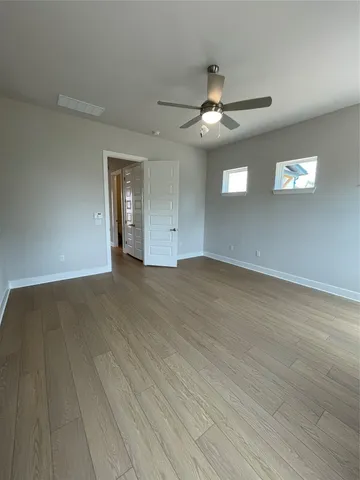 an empty room with wooden floor ceiling fan and windows