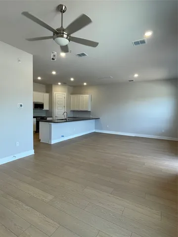 an empty room with wooden floor a ceiling fan kitchen view and a ceiling fan