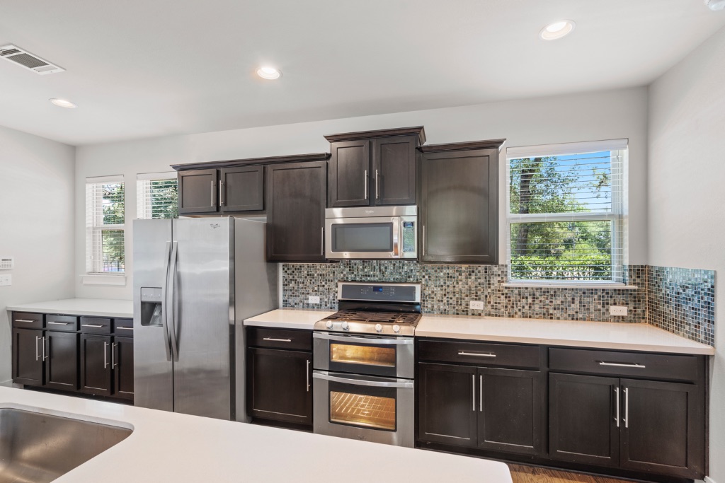 11229 Avery Station Loop, Unit 36 Austin, TX 78717 - Photo 10 of 37 Kitchen with stainless steel appliances, decorative backsplash, dark wood finish cabinets, recessed lighting, and light stone counters