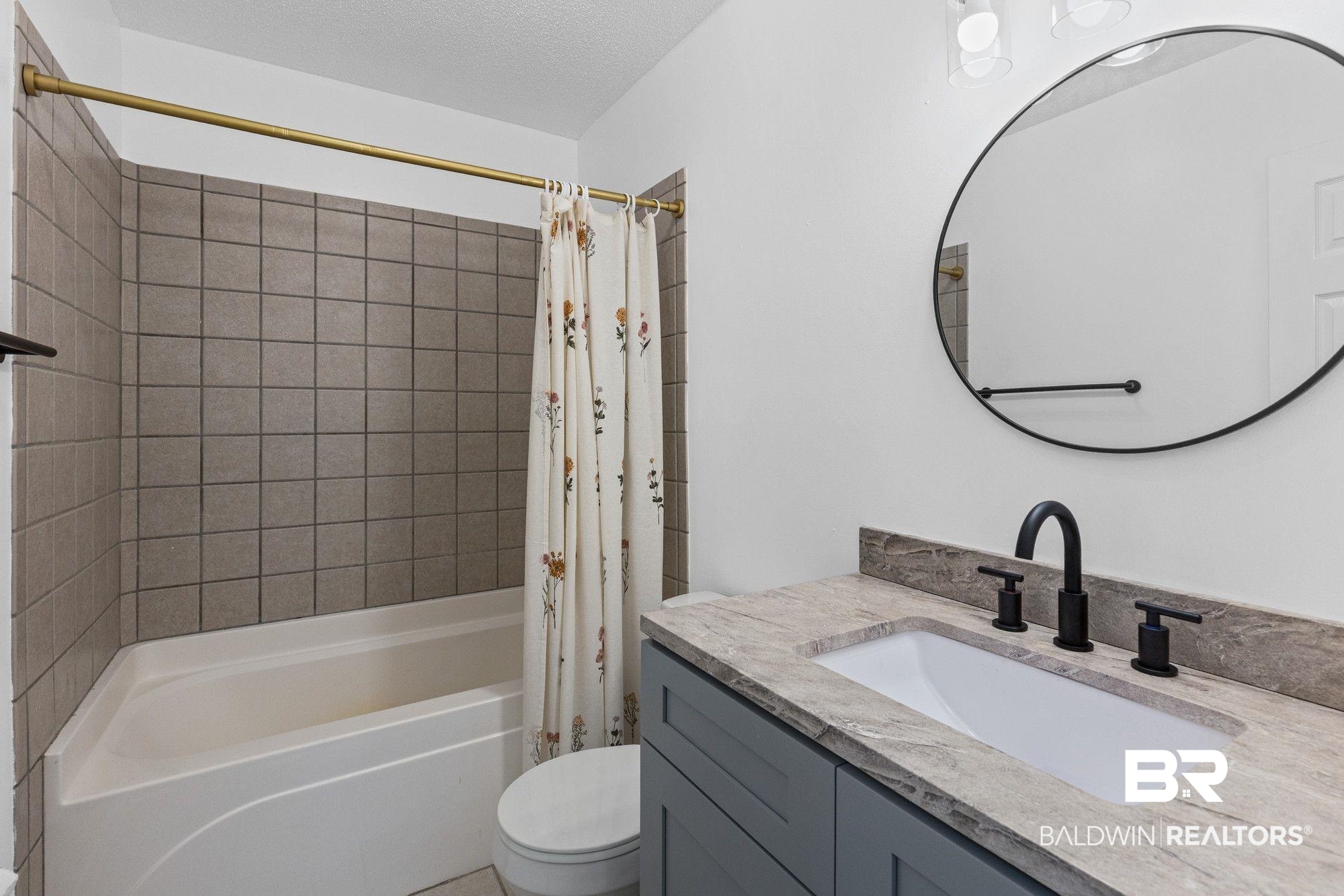 1301 Repoll Road Mobile, AL 36695 - Photo 15 of 21 Bathroom featuring a white bathtub with square gray tile surround, a gray vanity with a light gray countertop, a rectangular undermount sink, and a black faucet