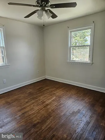 an empty room with wooden floor chandelier fan and windows