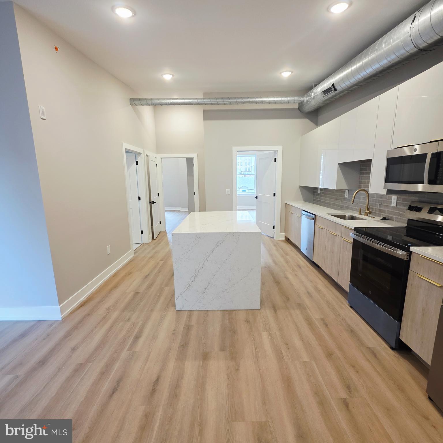 a large white kitchen with wooden floors and stainless steel appliances