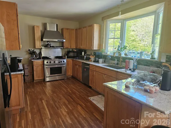 a kitchen with stainless steel appliances granite countertop wooden cabinets a stove a sink and a wooden floors