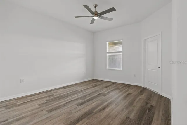 an empty room with wooden floor ceiling fan and windows