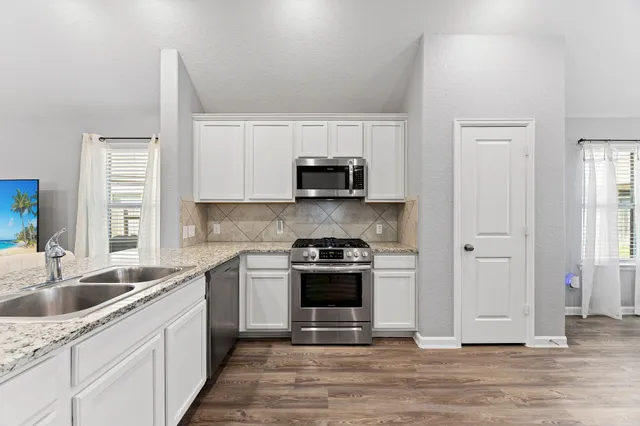 a kitchen with stainless steel appliances kitchen island granite countertop a dining table chairs and a refrigerator