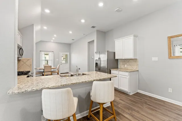 a kitchen with granite countertop a refrigerator oven a sink dishwasher and white cabinets with wooden floor