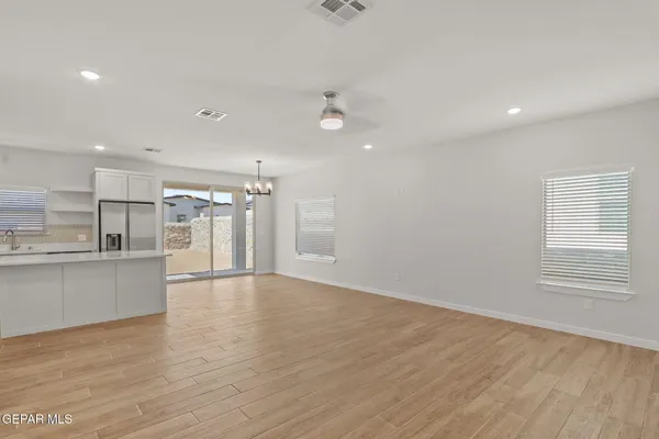 a view of an empty room and kitchen with wooden floor