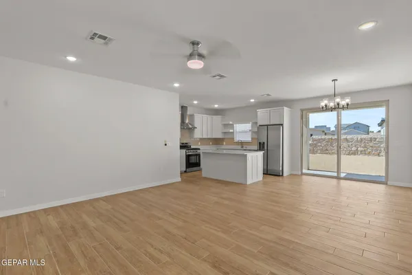 a view of an empty room with wooden floor and a kitchen