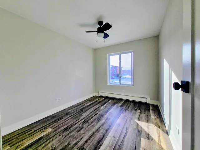 an empty room with wooden floor a ceiling fan and windows