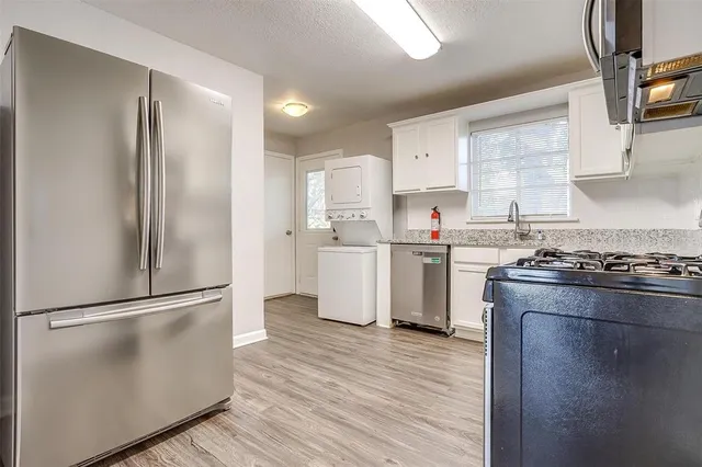 a kitchen with stainless steel appliances granite countertop a refrigerator a stove a sink and white cabinets with wooden floor