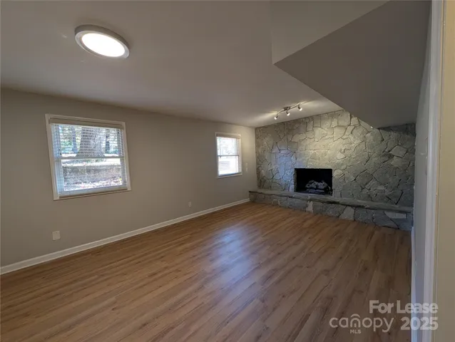 an empty room with wooden floor fireplace and windows