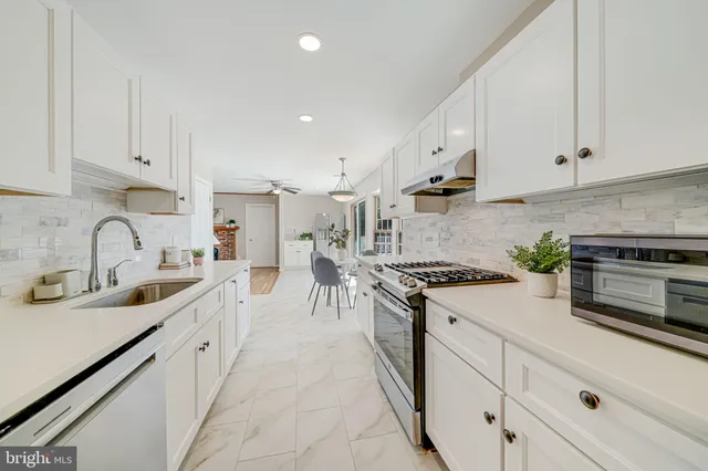 a large white kitchen with stainless steel appliances granite countertop a stove a sink a refrigerator and white cabinets