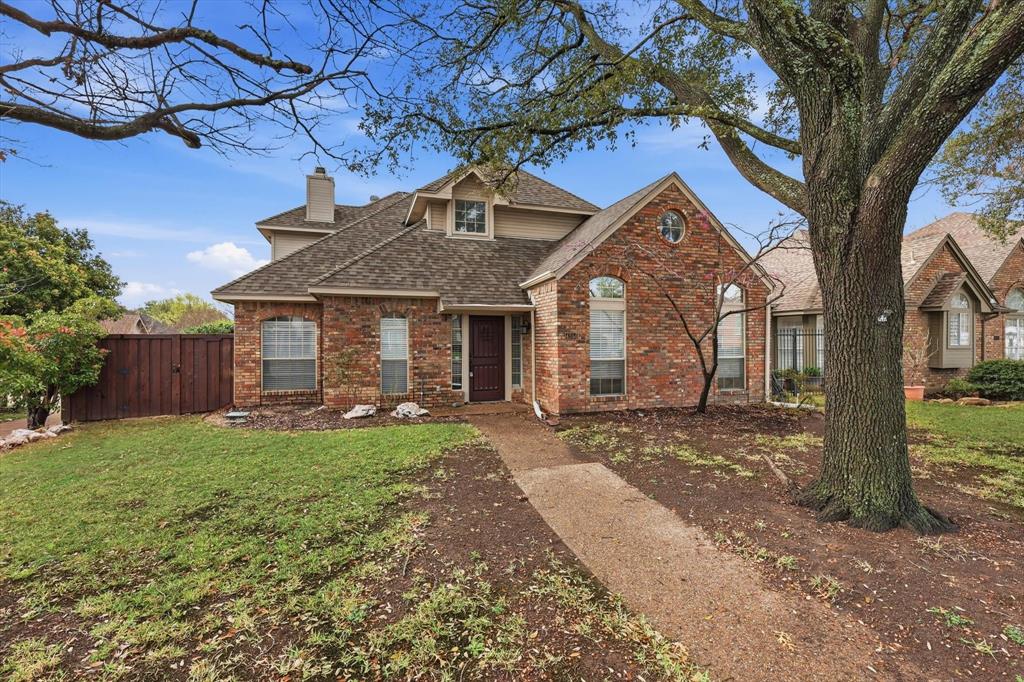 Traditional-style home with brick siding, a shingled roof, a chimney, and a gate