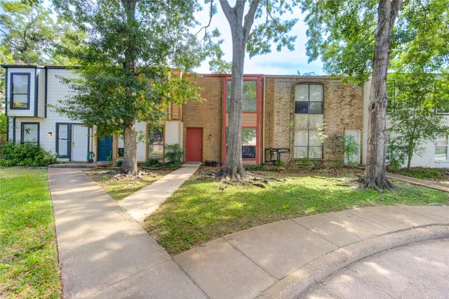 a view of a house with brick walls plants and large trees