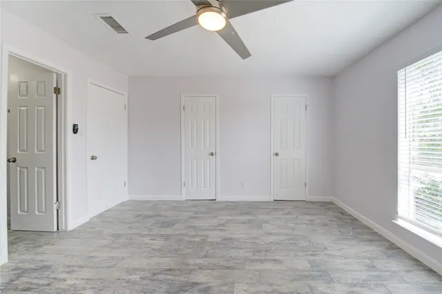 an empty room with wooden floor ceiling fan and windows