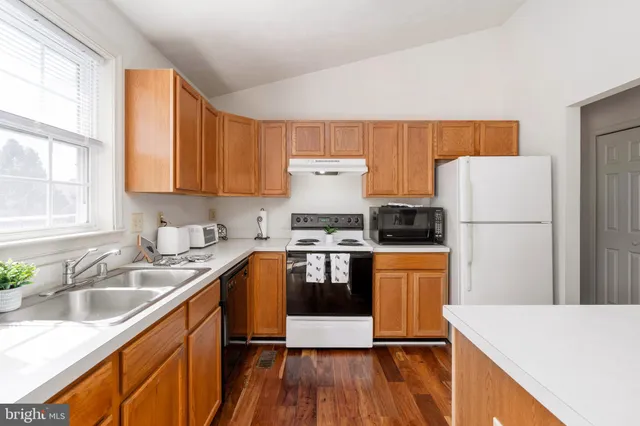 a kitchen with a refrigerator a stove a sink dishwasher and wooden cabinets with wooden floor