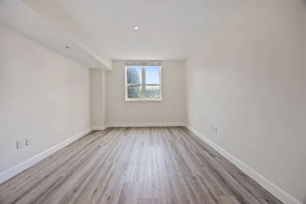 a view of an empty room with wooden floor and window