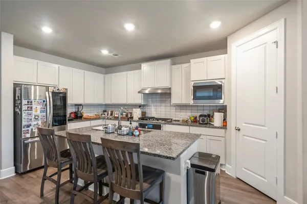 a kitchen with stainless steel appliances granite countertop a refrigerator a stove top oven a sink dishwasher and a refrigerator with wooden floor
