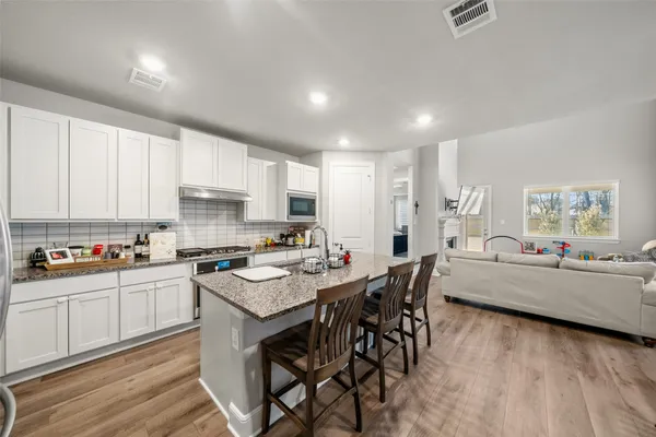 a kitchen with stainless steel appliances kitchen island granite countertop a stove a sink a refrigerator and white cabinets with wooden floor