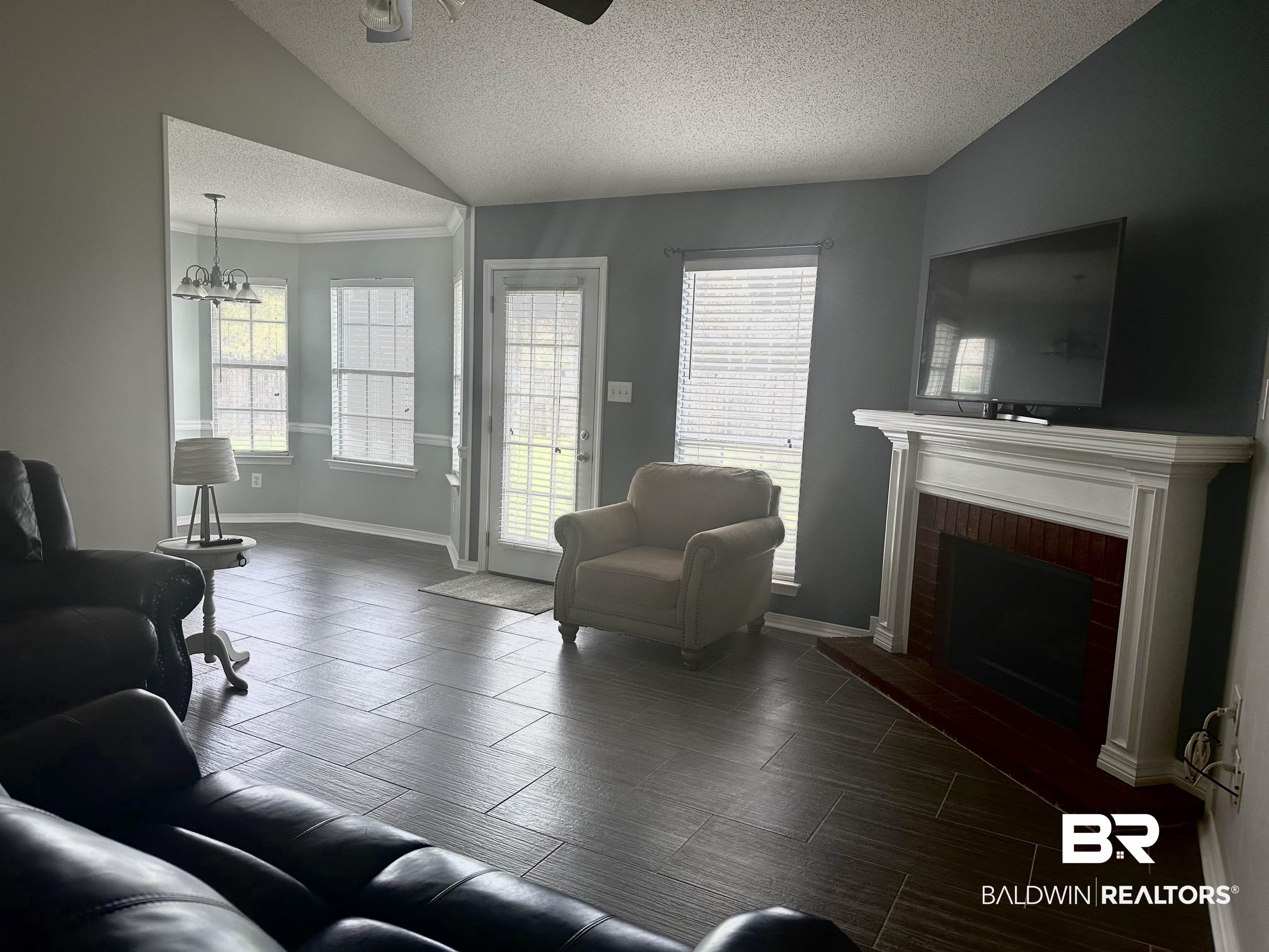 4882 Rebecca Place Mobile, AL 36695 - Photo 29 of 29 Living room with a brick fireplace, baseboards, vaulted ceiling, ceiling fan with notable chandelier, and a textured ceiling
