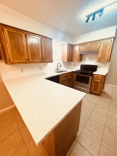 102 Verna Spur, Unit A Georgetown, TX 78628 - Photo 18 of 20 Kitchen featuring stainless steel range, light tile patterned floors, a textured ceiling, a peninsula, and brown cabinets
