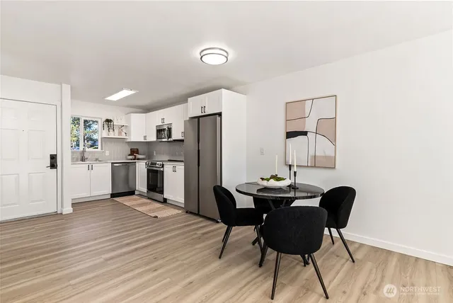 a kitchen with stainless steel appliances kitchen island granite countertop a dining table chairs and a refrigerator