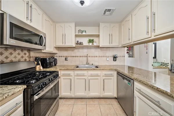 a kitchen with stainless steel appliances granite countertop a stove top oven a sink dishwasher and white cabinets