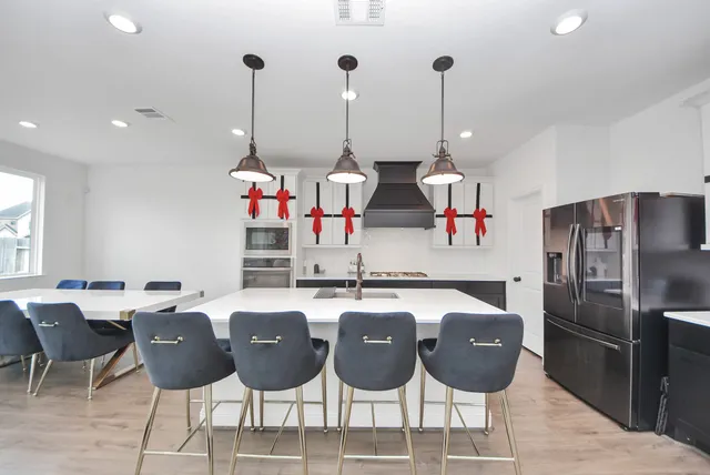 a kitchen with stainless steel appliances kitchen island granite countertop a dining table chairs and a refrigerator